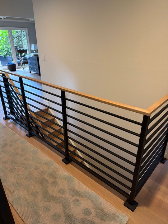 Modern staircase railing with horizontal black metal bars and wood handrail in a home interior