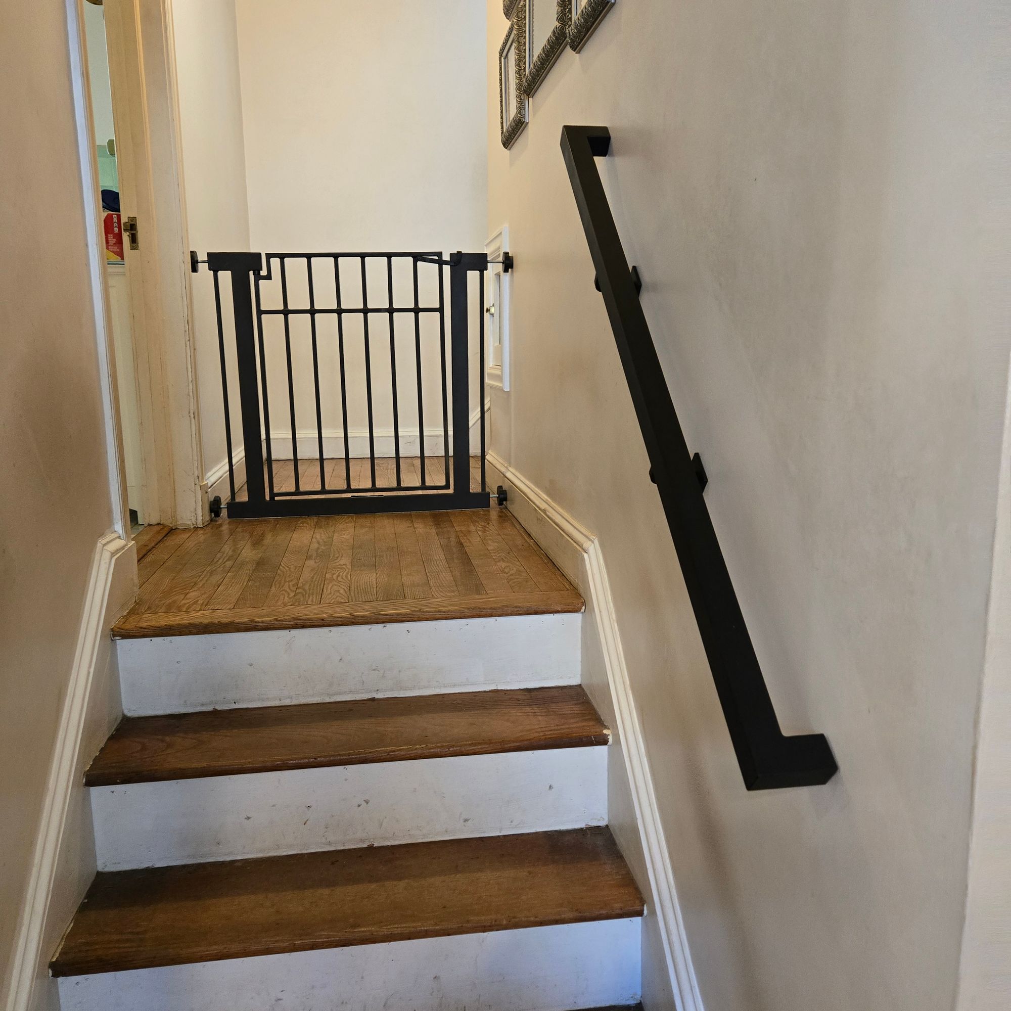 Interior staircase with wooden steps, white risers, black handrail, and safety gate at the top landing