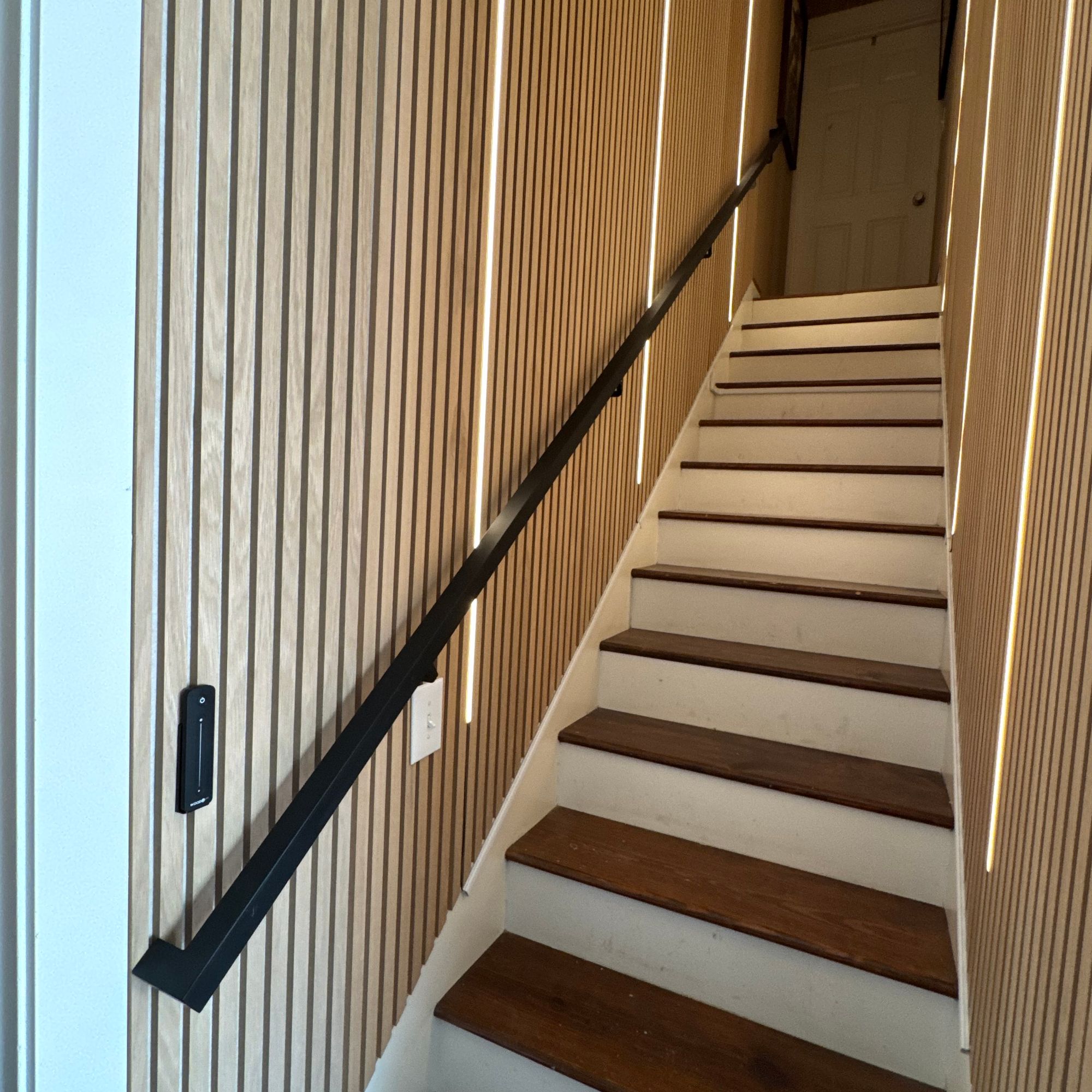 Modern wooden staircase with vertical wood slat wall paneling and black handrail leading to upper floor