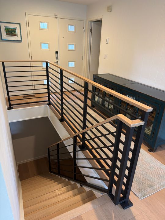 Modern staircase with black metal railings and wood handrails leading to upper floor, with front door visible in background