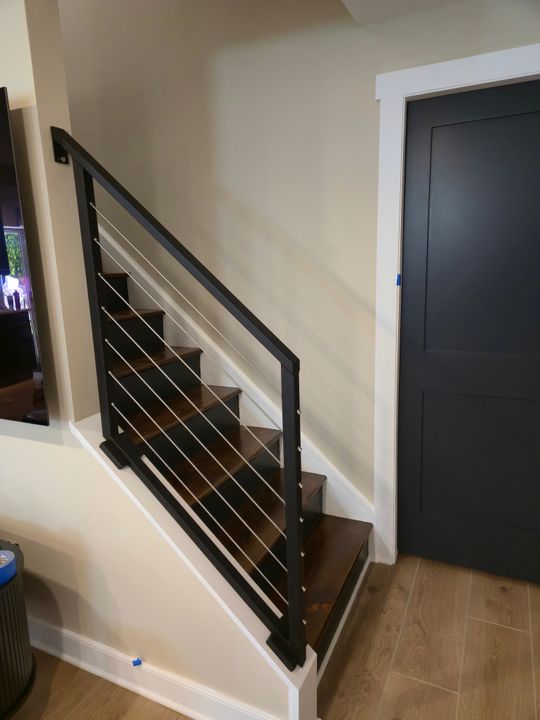 Modern staircase with black metal horizontal railings and wood steps leading upstairs, with a dark door visible on the right side