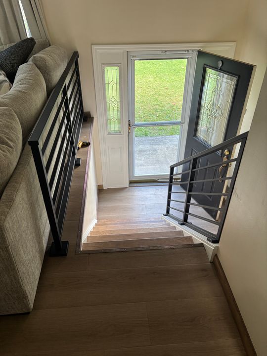 Interior view of a staircase with black metal railings leading down to an entryway with a white front door featuring decorative glass panels and sidelights, showing a green lawn outside