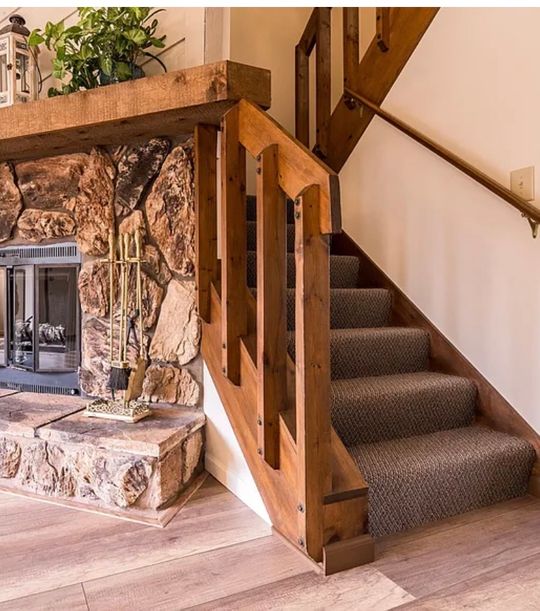 Rustic interior with wooden staircase, stone fireplace, and carpeted steps in a cozy home setting