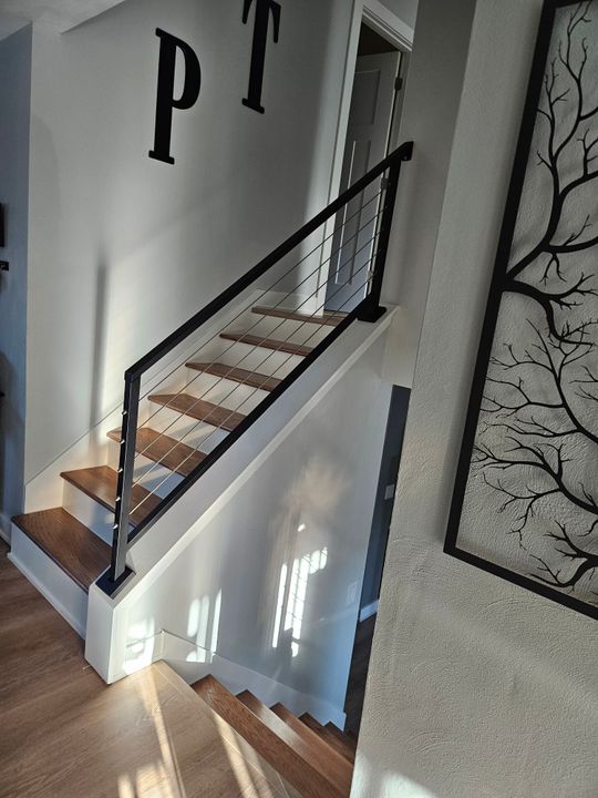 Modern staircase with wooden steps, black metal cable railing, white walls, and decorative tree branch artwork