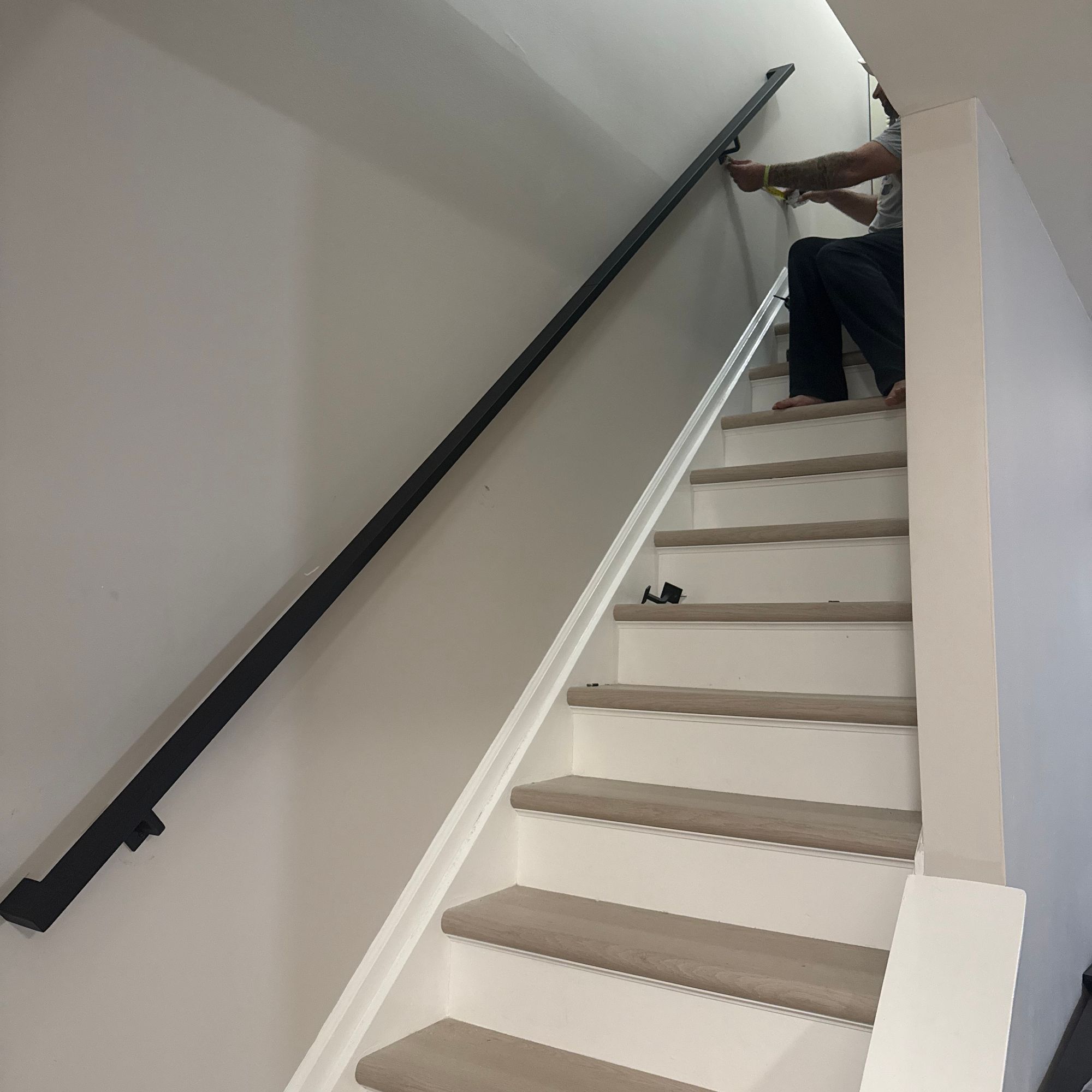 Person installing a black handrail on white stairs with wooden treads
