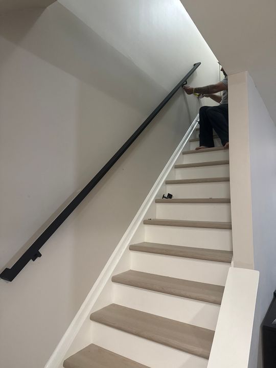 Person installing a black handrail on white stairs with wooden treads