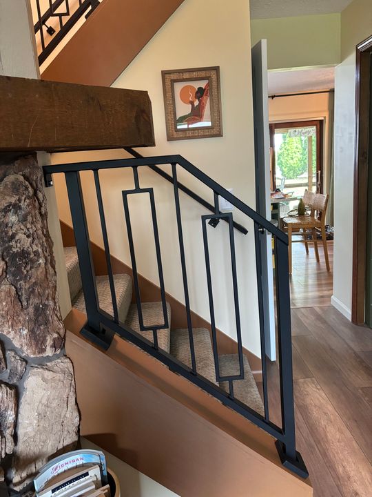 Interior staircase with black metal railing, wooden steps, stone fireplace, and view into adjacent dining room with hardwood floors