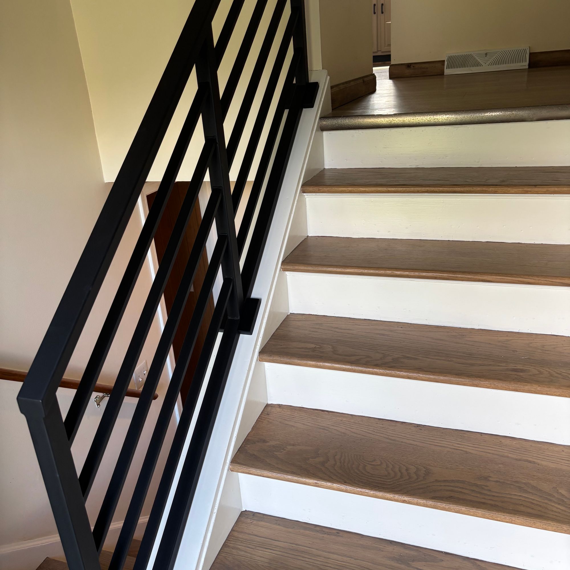 Modern staircase with wooden treads, white risers, and black metal geometric railing leading to upper floor
