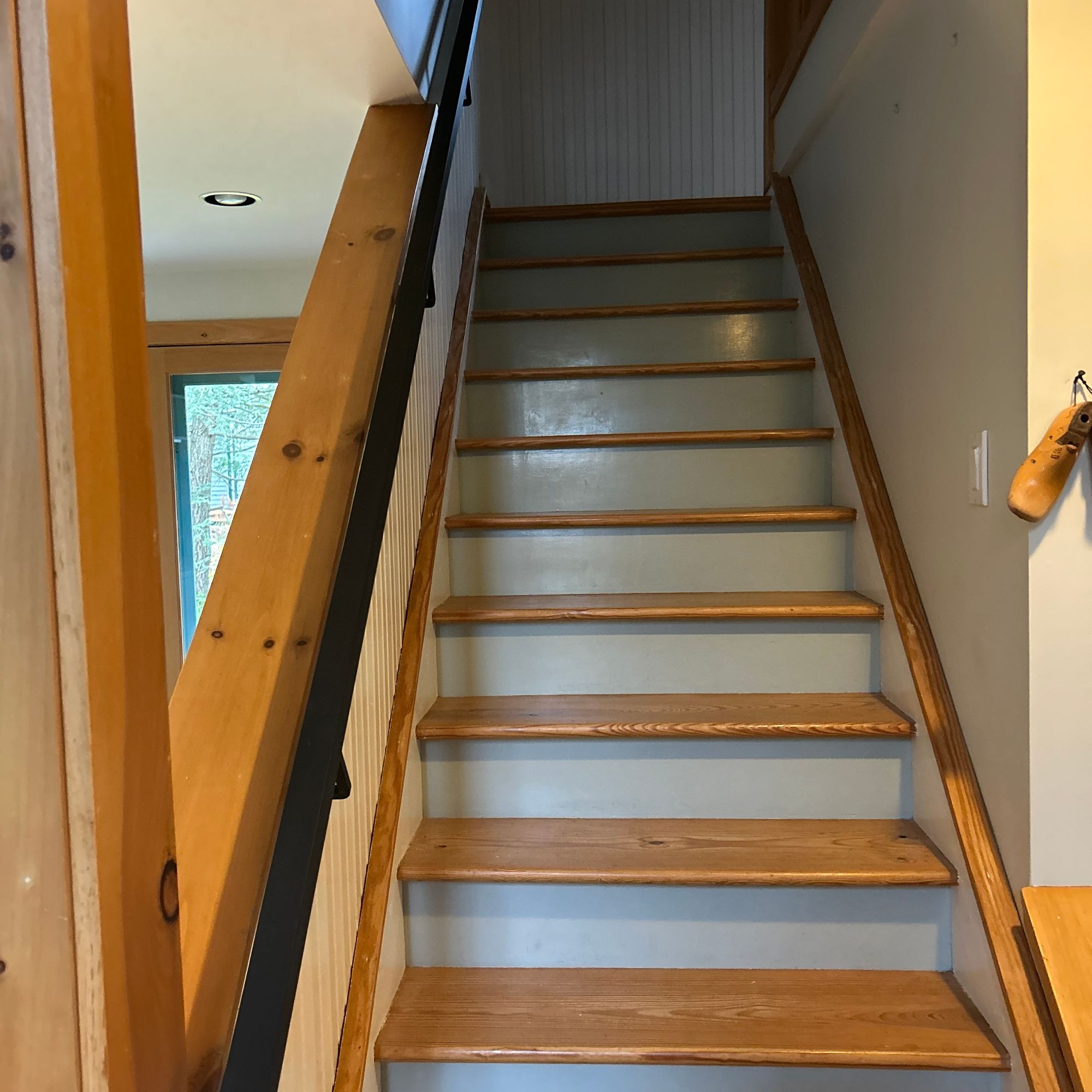 A wooden staircase with natural wood treads and white risers, featuring a black handrail and wooden balusters, leading to an upper floor in a home interior.