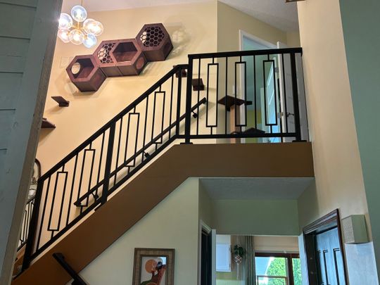 Modern interior staircase with black metal railings, decorative hexagonal wall shelves, and contemporary lighting fixture in an open-concept home