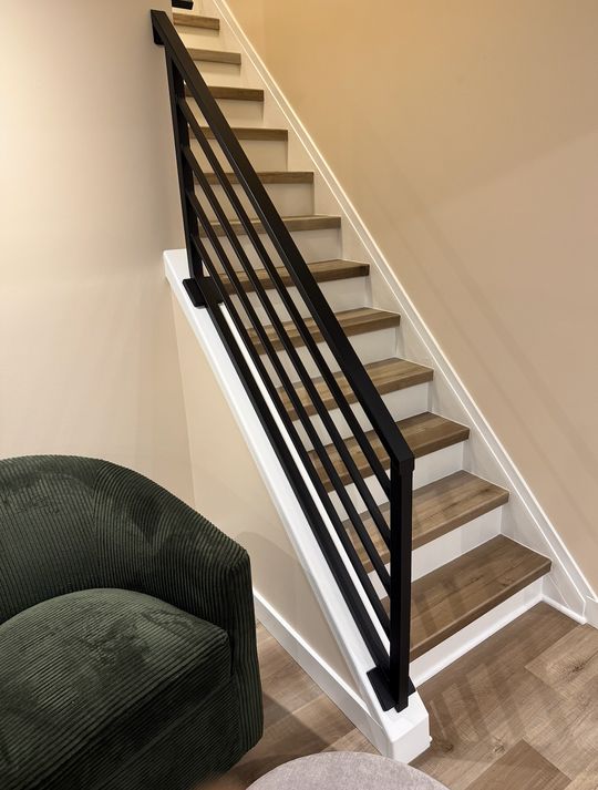 Modern staircase with black metal railings, white risers, and wood treads next to a green upholstered chair