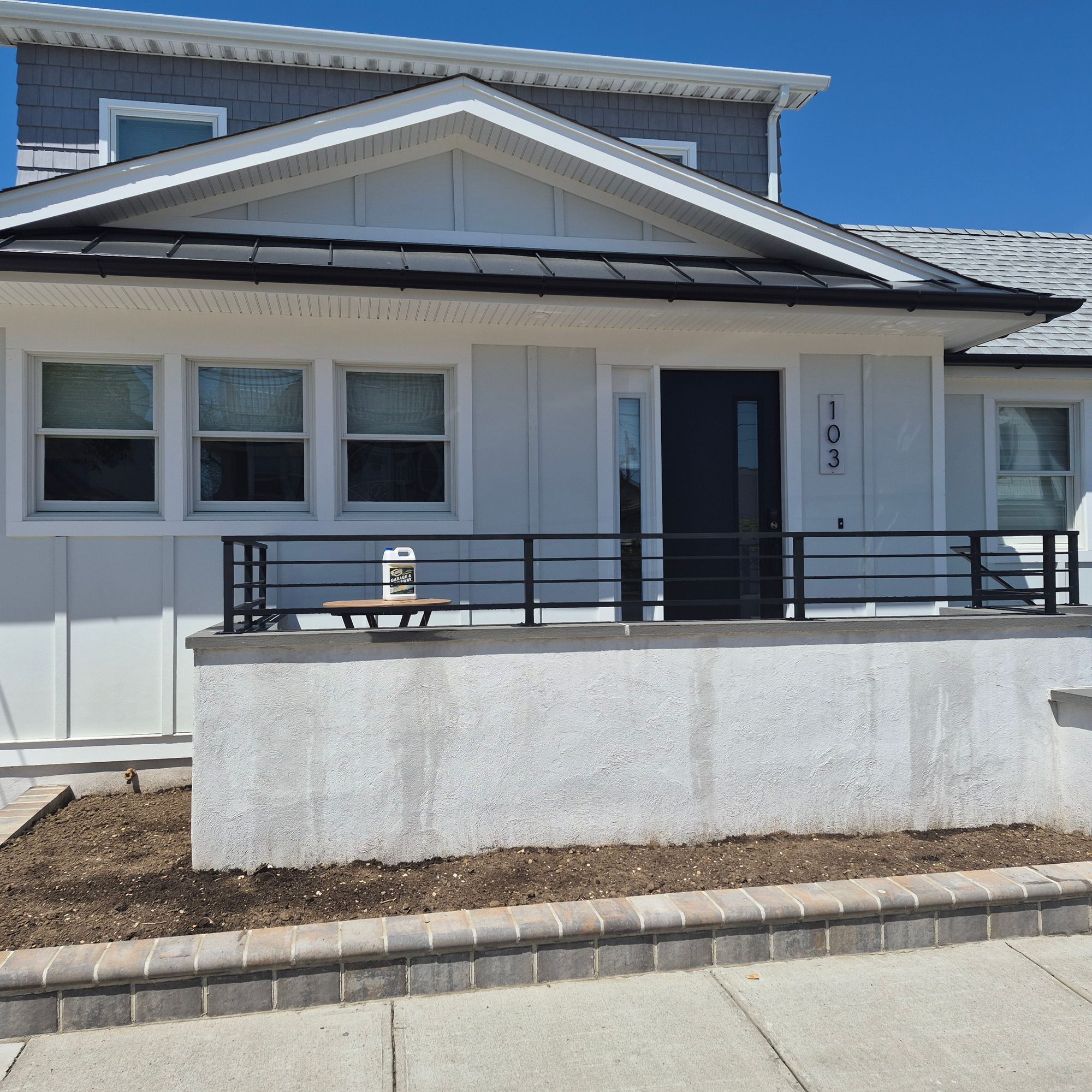 Modern single-story house with white and gray exterior, solar panels on roof, front porch with metal railing, and landscaped front yard with brick edging