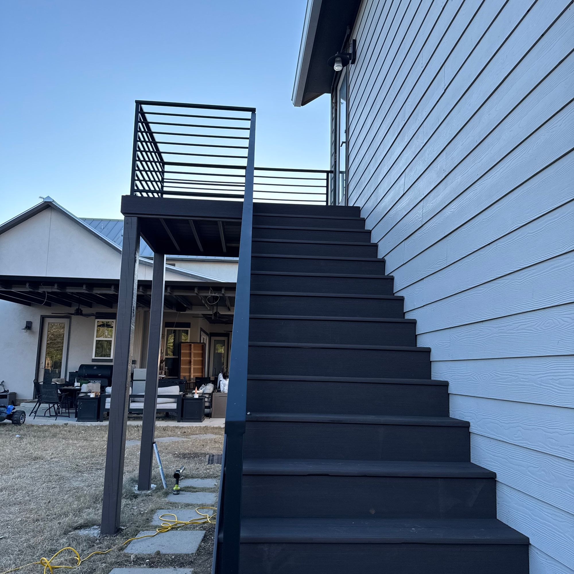 Modern black metal staircase with horizontal railing leading to upper level of white siding house exterior