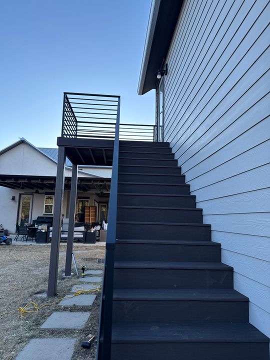 Modern black metal staircase with horizontal railing leading to upper level of white siding house exterior