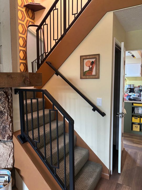 Interior staircase with black metal railings, carpeted steps, and decorative wallpaper featuring hexagonal patterns