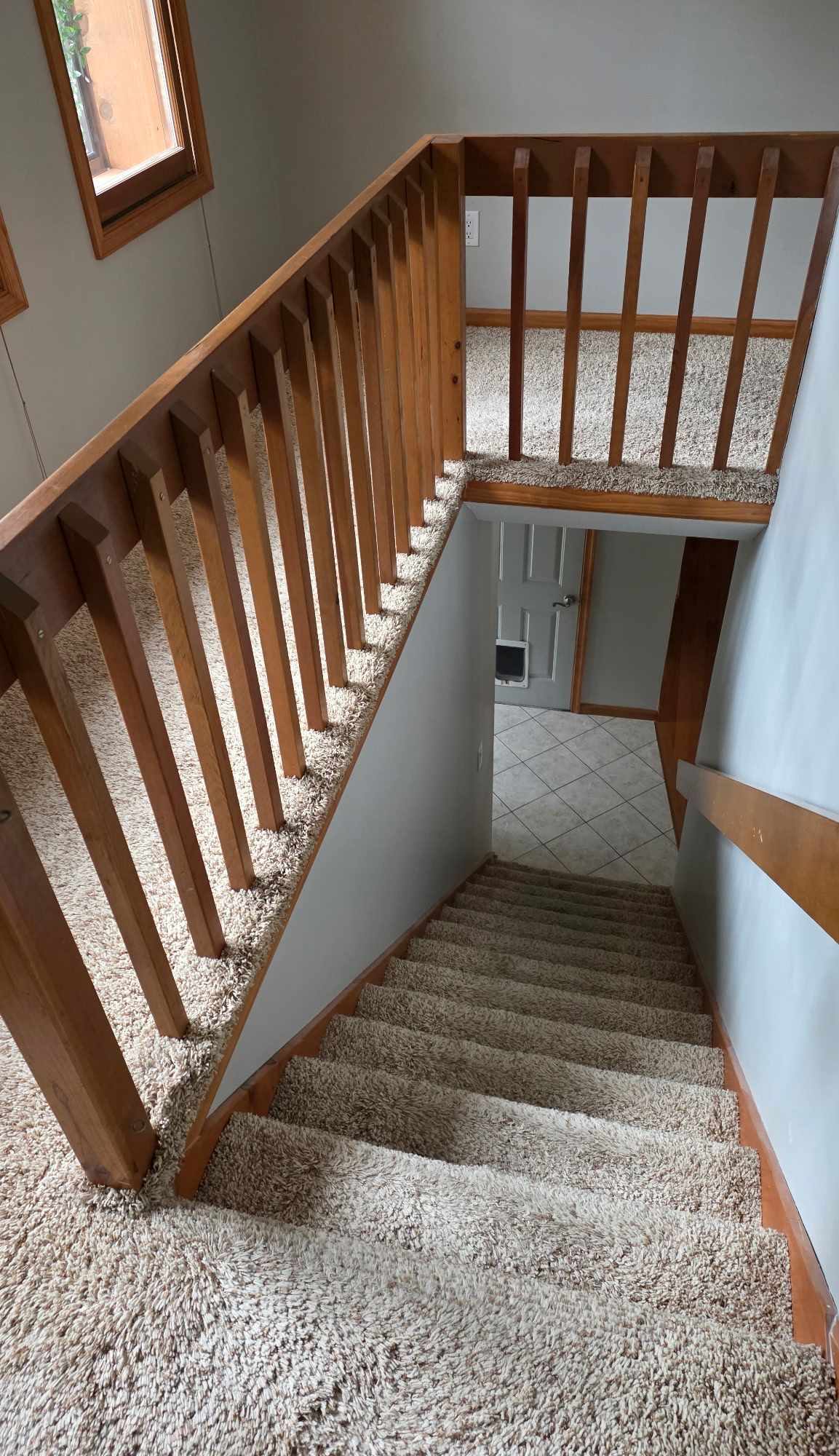 Carpeted staircase with wooden handrail and balusters leading down to a tiled floor area