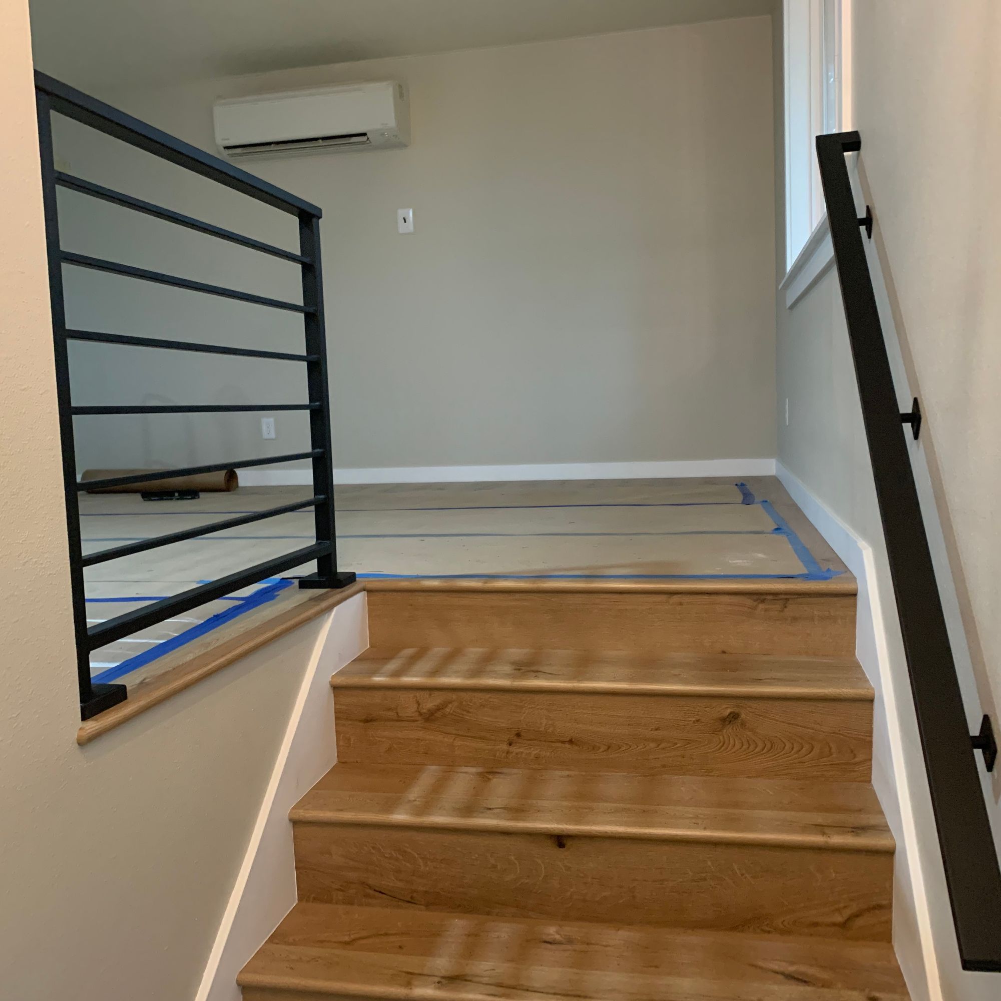 Modern wooden staircase with black metal railings leading to an upper floor with white walls and air conditioning unit