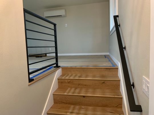 Modern wooden staircase with black metal railings leading to an upper floor with white walls and air conditioning unit