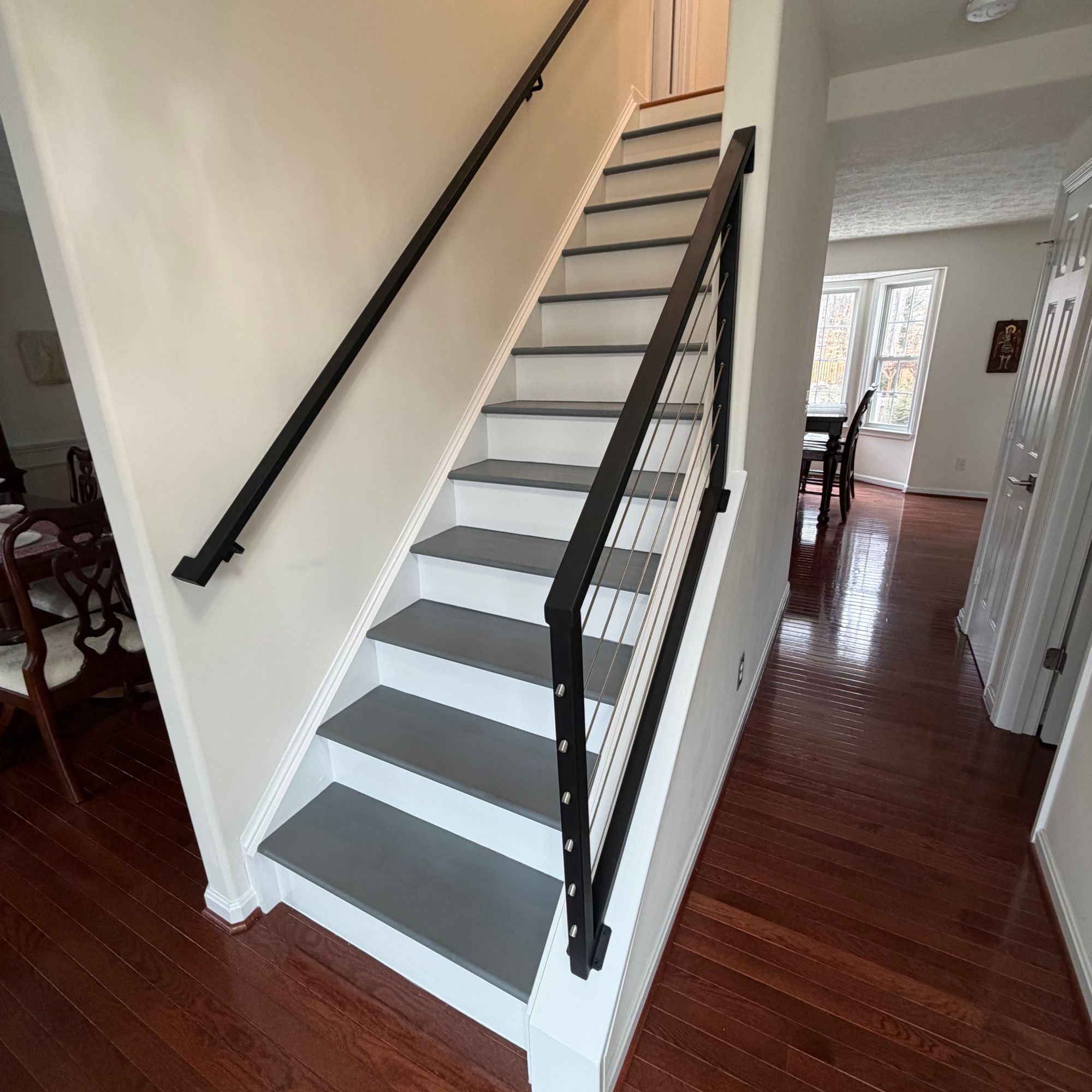 Modern staircase with white risers, gray treads, and black metal railing in a home interior with dark hardwood floors