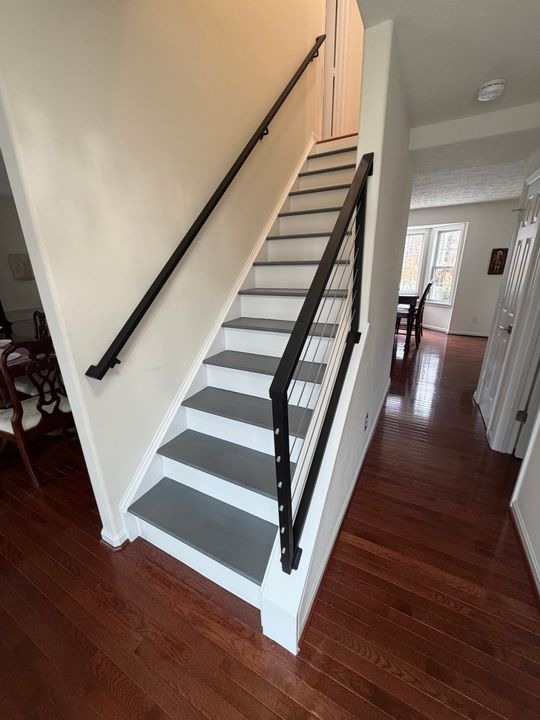 Modern staircase with white risers, gray treads, and black metal railing in a home interior with dark hardwood floors