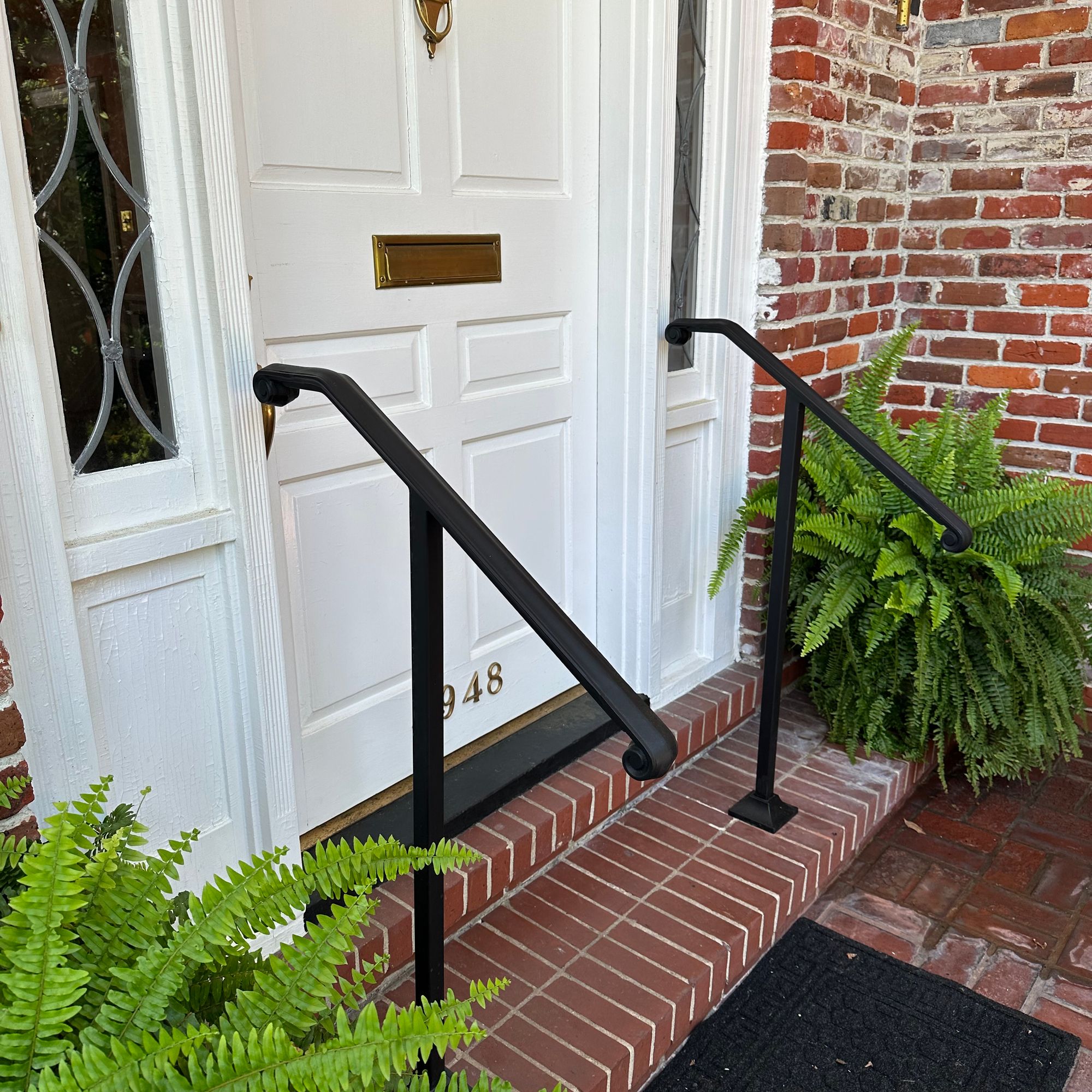 Front entrance of a brick home with white door, black handrails, brick steps, and green ferns