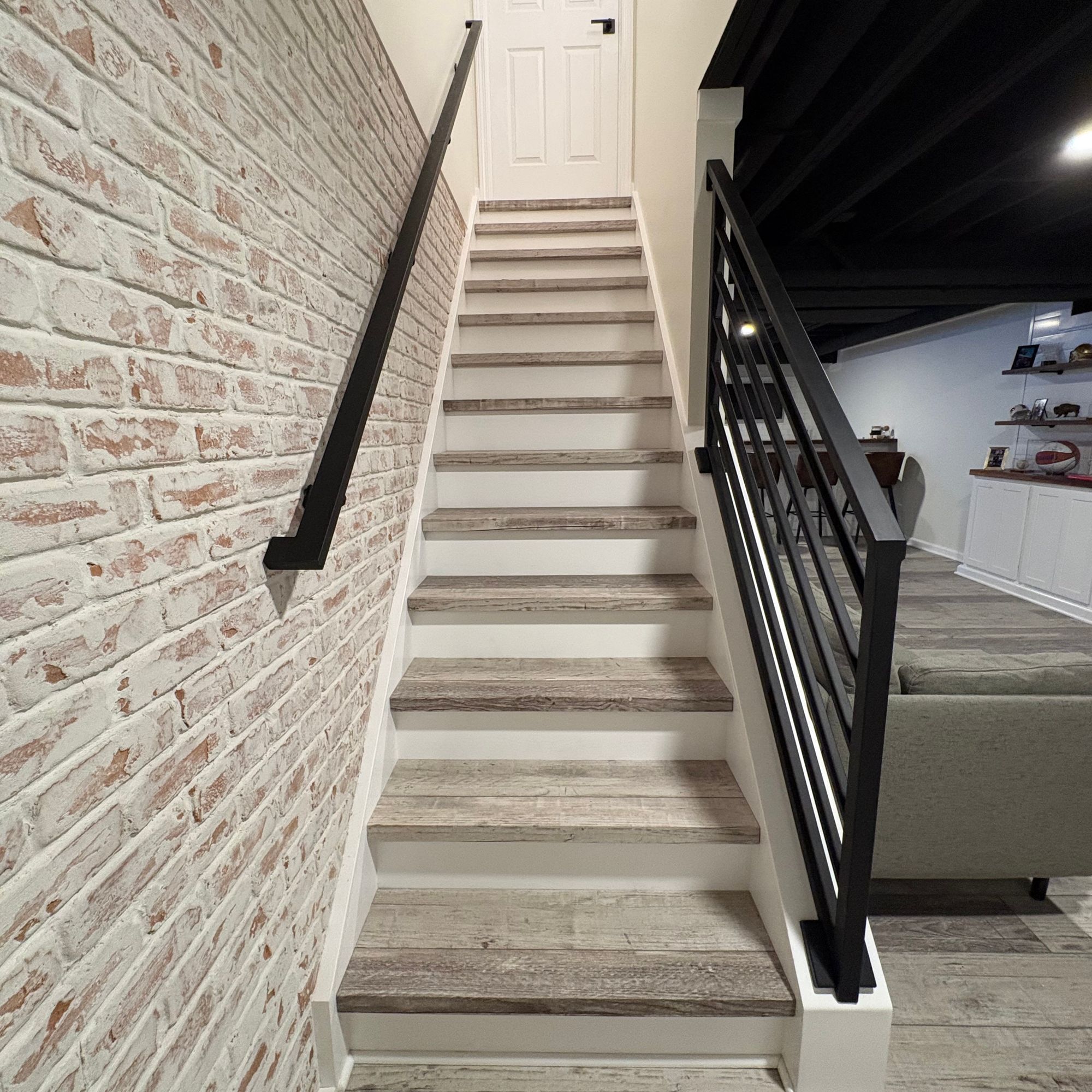 Modern staircase with white risers, wood treads, black metal railing, and exposed brick wall in contemporary home interior