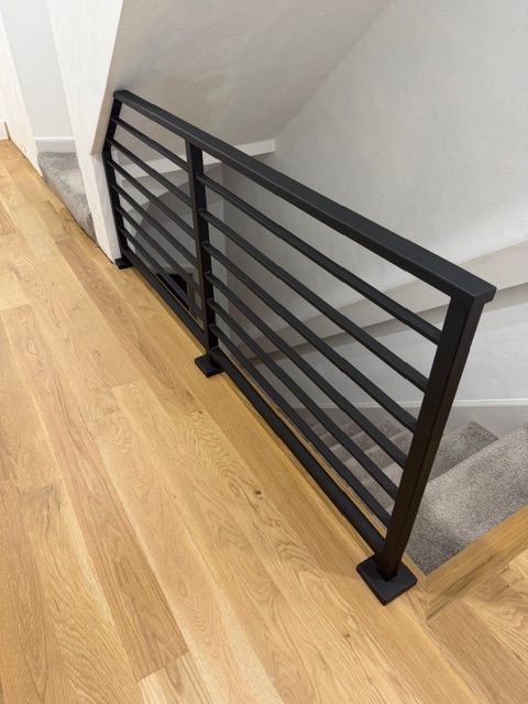Modern black metal stair railing with horizontal slats on wooden flooring in white-walled interior