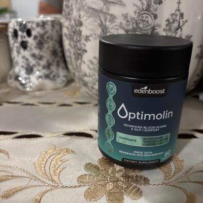 Customer-uploaded image. Click to see more details. The image represents: A container of Edenboost Optimolin dietary supplement for advanced blood sugar and GLP-1 support, displayed on a decorative white tablecloth with gold embroidered floral patterns. Decorative items and patterned home décor are visible in the blurred background.