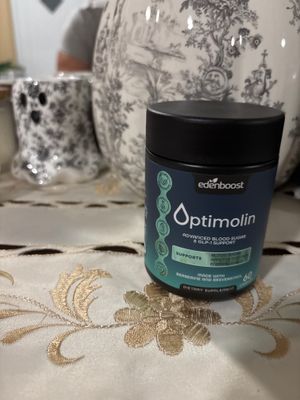 Customer-uploaded image. Click to see more details. The image represents: A container of Edenboost Optimolin dietary supplement for advanced blood sugar and GLP-1 support, displayed on a decorative white tablecloth with gold embroidered floral patterns. Decorative items and patterned home décor are visible in the blurred background.