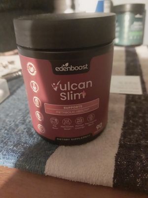 Customer-uploaded image. Click to see more details. The image represents: A red and black cylindrical dietary supplement container labeled "edenboost vulcan slim" that supports metabolic health, displayed on a textured fabric surface with other items blurred in the background.
