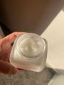 A hand holding an open glass jar containing white cream or moisturizer product