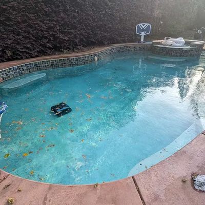 A pool with autumn leaves on the surface and a robotic pool cleaner