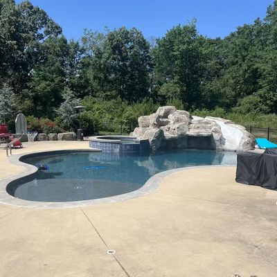 Backyard swimming pool with rock waterfall feature and concrete deck