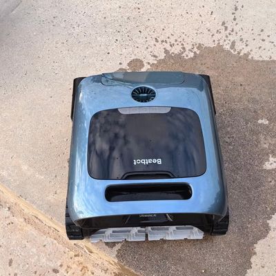 A blue and black robotic pool cleaner on concrete poolside pavement