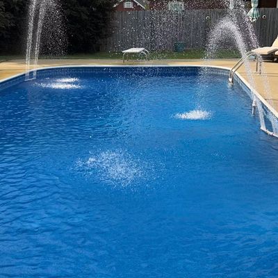 A backyard pool with bright blue water and multiple water fountains spraying