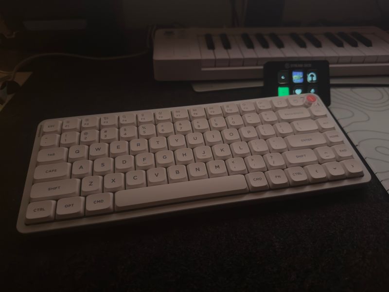 Customer-uploaded image. The image represents: White wireless keyboard on a desk with a laptop screen visible in the background showing app icons