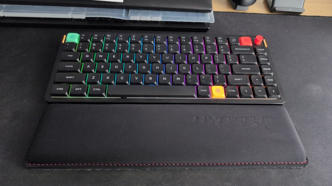 Customer-uploaded image. The image represents: A compact mechanical keyboard with RGB backlighting sits on a black gaming mouse pad on a dark desk surface