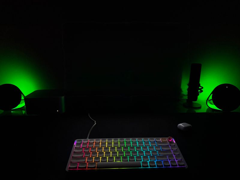 Customer-uploaded image. The image represents: Gaming setup with RGB backlit keyboard, computer mouse, and green ambient lighting in dark room