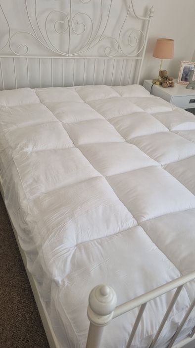 A customer's queen bed on a white iron frame, the topper's quilted squares plump across the whole mattress
