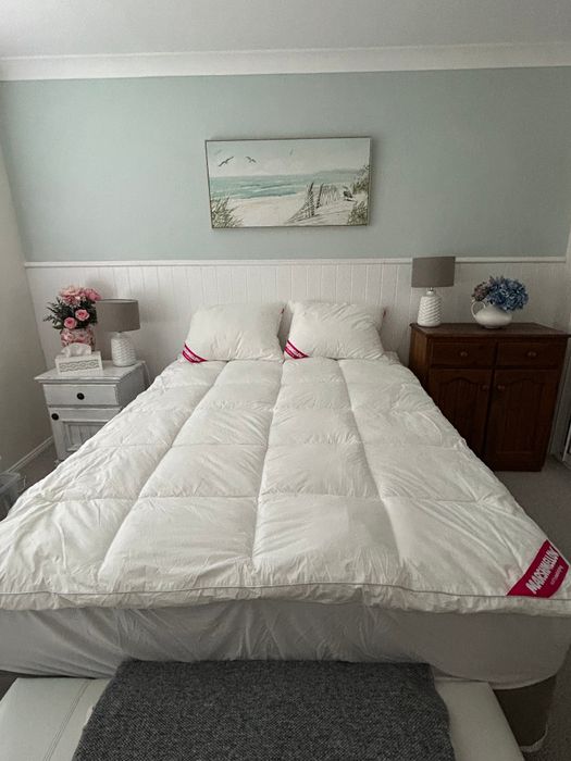 A customer's queen bed in a pale blue room, the topper and two pillows under a beach print