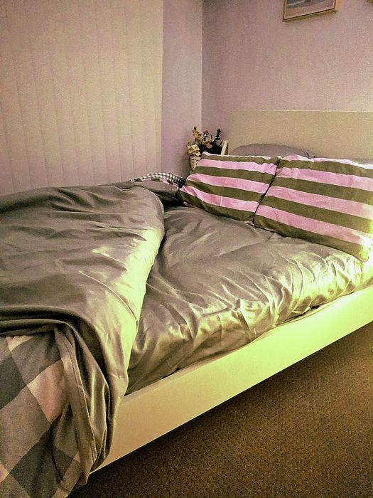 A customer's queen bed in a rented room, the topper under a grey quilt and two striped pillows