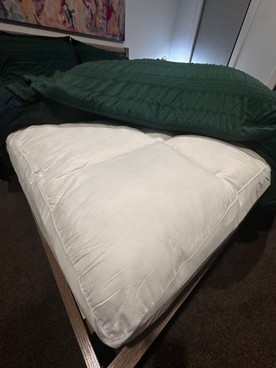An owner's queen bed with the topper folded back at the corner, showing how thick the plush layer is