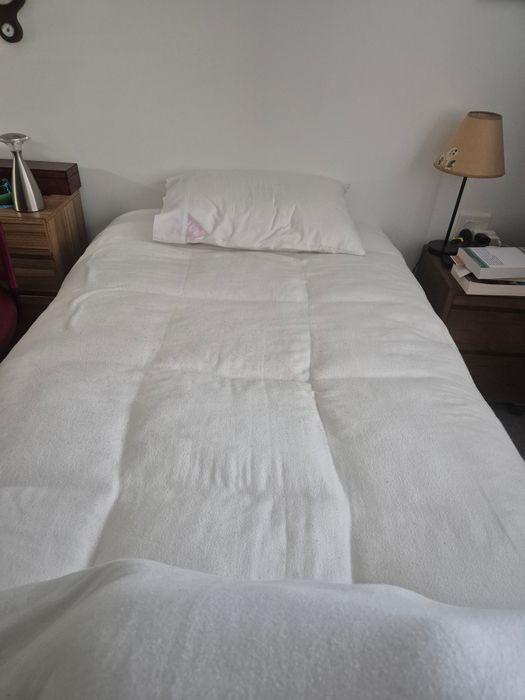 A customer's king single bed between two bedside tables, made up with the topper and a pillow