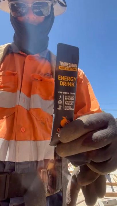 A worker in orange hi-vis and a face covering holding up an Energy Drink sachet on site