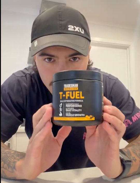 Person wearing a cap holding a container of T-FUEL supplement product