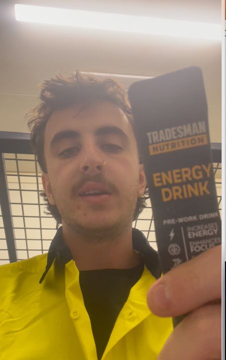 A young man in a yellow hi-vis shirt holding up an Energy Drink sachet