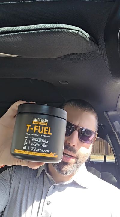 A man with sunglasses and facial hair sitting in a car holding a container of T-Fuel nutritional supplement