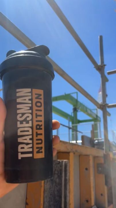 A Tradesman Nutrition shaker held up against blue sky and scaffolding on a building site