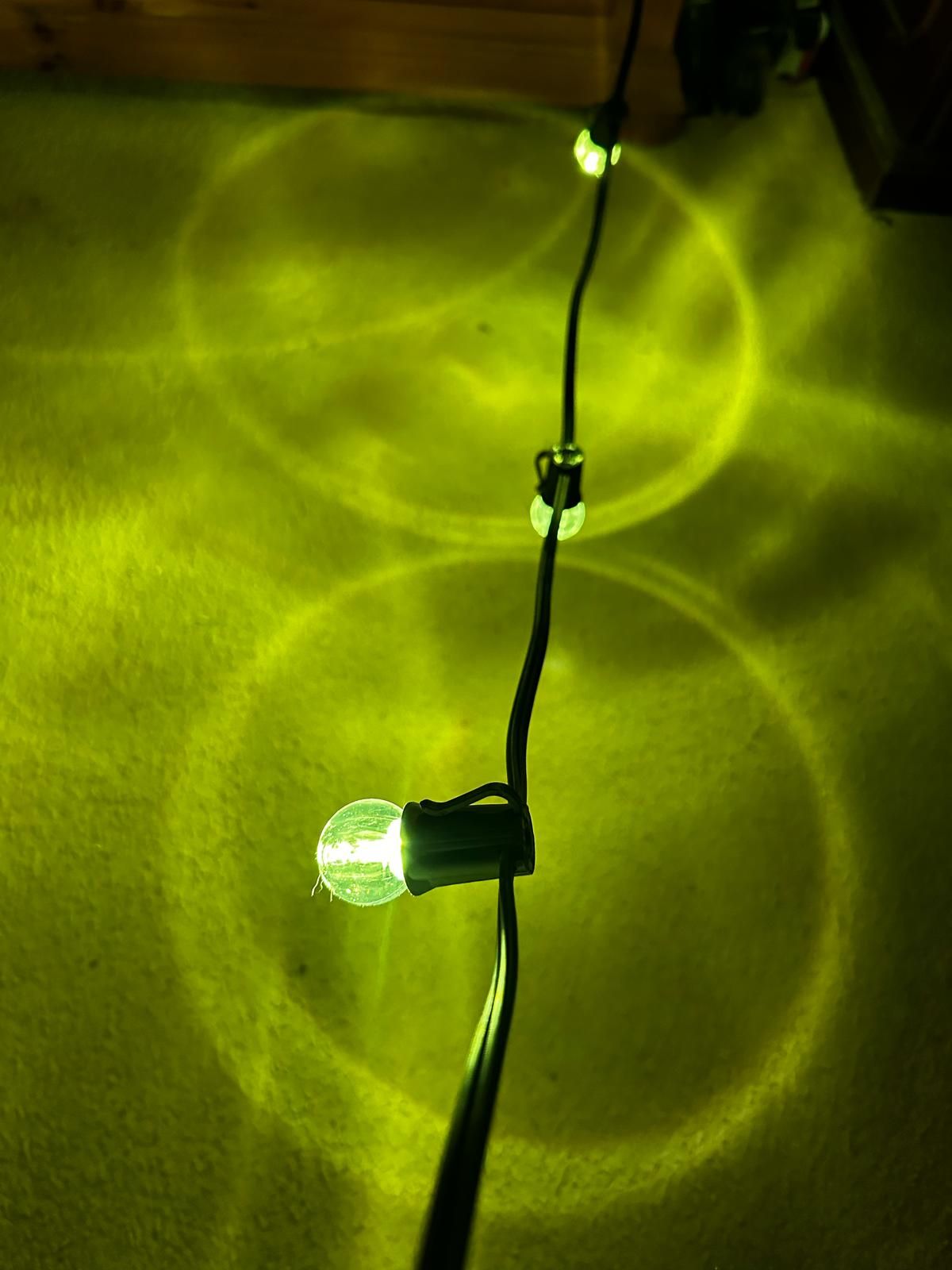 Green LED lights on a cable creating circular light patterns and shadows on a textured surface