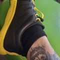 Person wearing black athletic shoe with yellow sole, showing tattooed leg while sitting on green chair